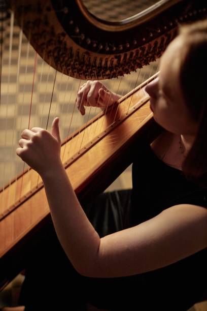 istock Woman Playing Harp Plucking Strings Gently while Performing Music Indoors 2193593655