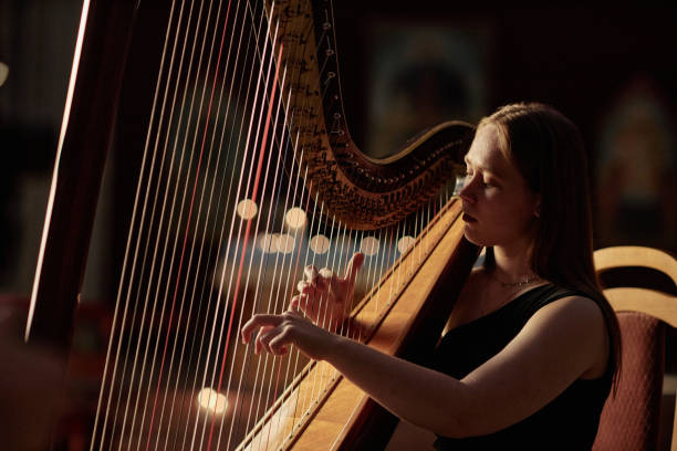istock Young Woman Strumming Harp Strings Playing Classical Music in Dim Light Indoors 2193593659