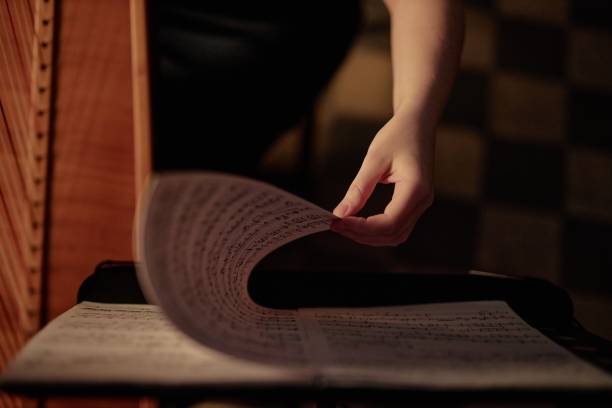 istock Female Hand Turning Page with Music Notes while Playing Harp in Low Key Light Indoors 2193593667