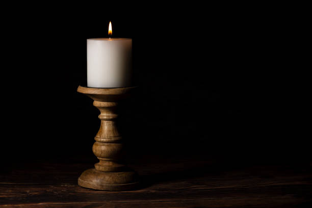 Lit candle on a wooden holder in low light. Warm candle glow.
