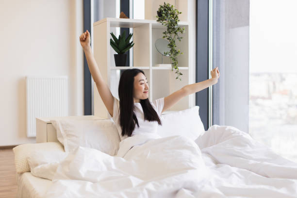 istock Asian woman joyfully stretching in bed during sunny morning 2193619916