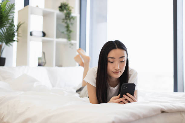 istock Young Asian woman on bed using smartphone for messaging 2193619954