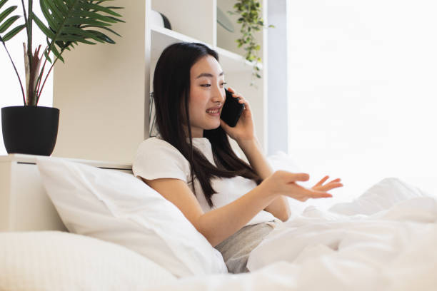 istock Asian woman enjoying a phone conversation while relaxing in bed at home 2193619955