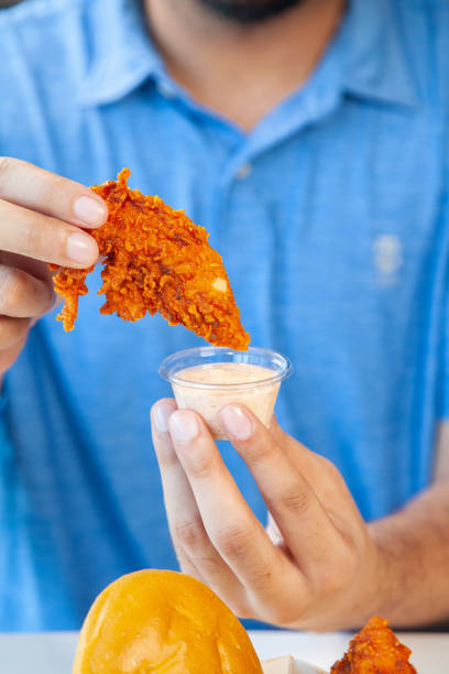 istock Man holding fried chicken strip dunking in spicy mayo sauce. 2193634938