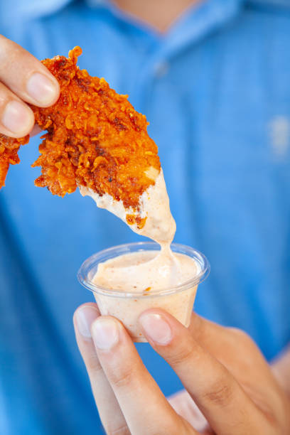 Man holding fried chicken strip dunking in spicy mayo sauce.