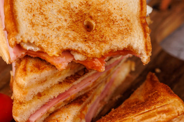 istock Tasty Egg, Ham, and Cheese Sandwich Partially Eaten with Cherry Tomatoes on Dark Board 2193636475