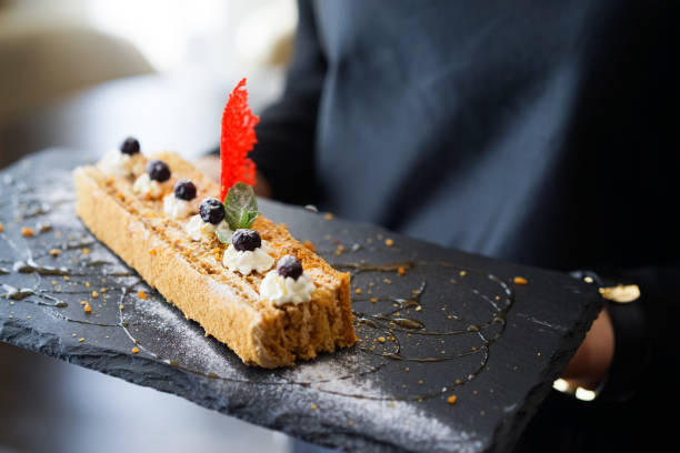 A delicately plated gourmet dessert garnished with cream, berries, honey drizzle, and a decorative sugar element, served on a stylish slate plate, representing exquisite culinary presentation and fine dining experience.
