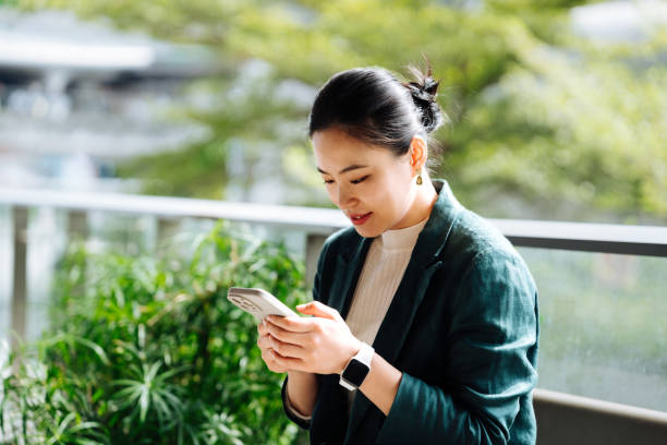 istock Asian business woman using smartphone working on digital tablet in business park. Taking a break from work. Remote working with flexibility. Working outdoors with technology. Business lifestyle. Work-life balance and wellbeing concept . 2193641524