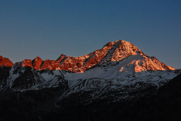 Aerial view of sun rise over snowcapped mountains and icy ridge of mountain peak in foreground, Swiss Alps