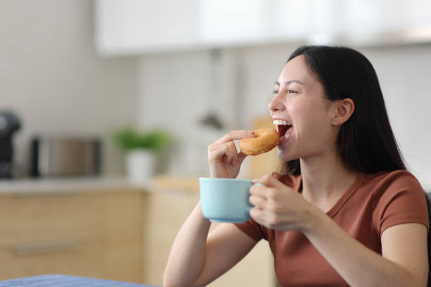 Asian woman eating doughnut drinking coffee