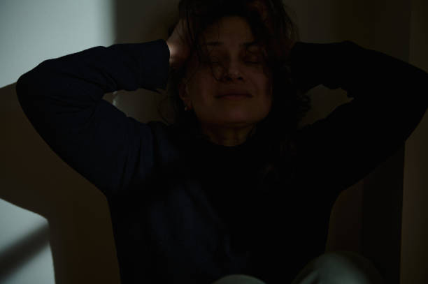 istock Woman distressed in low-light room holding her head 2193649109