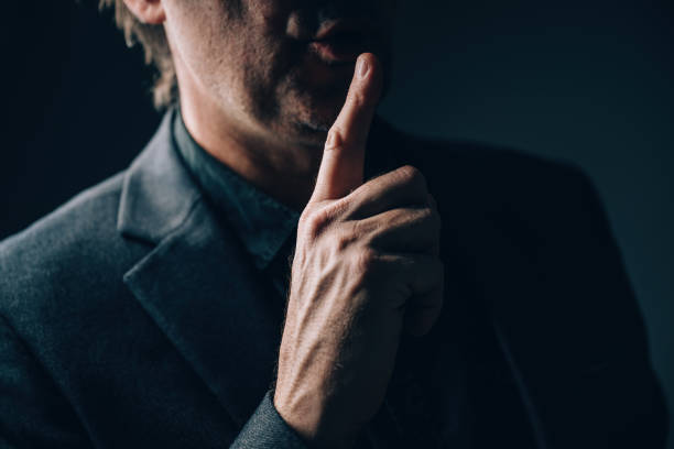 istock Businessman making a shh hand sign gesture, be quiet and keep the business secrete. Close up low key portrait of entrepreneur holding a finger on lips 2193655844