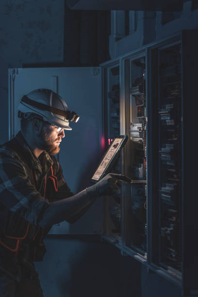 istock Electrician in overalls, focused on work in switchboard with fuses, using tablet. 2193656166
