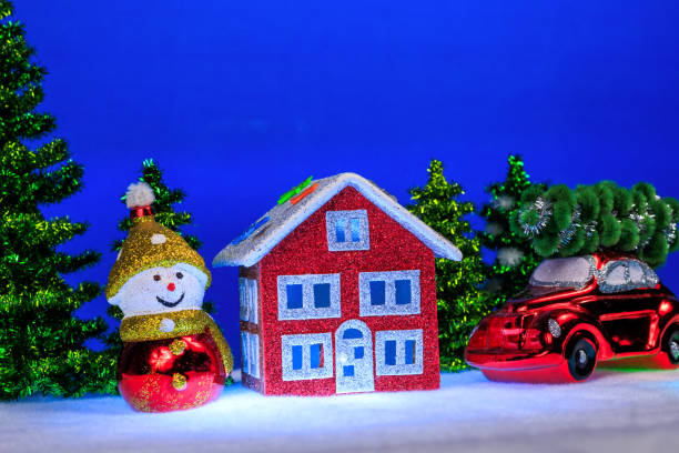 On a blue background, a red house with blue light in the windows, surrounded by a snowman and a red car with a Christmas tree on the roof