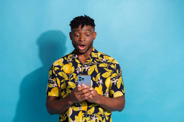 istock Young man in stylish shirt looking surprised while using smartphone on bright blue background 2193657575