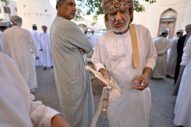 Nizwa, Oman - October 25, 2024: Unidentified Omani men in traditional costumes selling guns at Nizwa gun market, Oman
