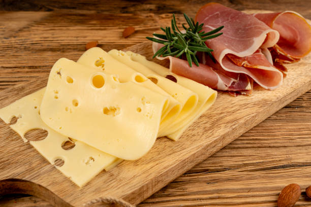 Cheese plate with prosciutto, jamon cut, parma ham, dry serrano slices, cured iberico closeup, cheese board, assorted chopped dairy products, many stinky French cheeses on wood