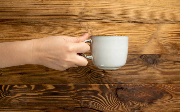 istock Hand Holds Cup, Empty Cup in Hands, Coffee Mug, Teacup Mockup, Cup in Arms on Wooden Table 2193667633