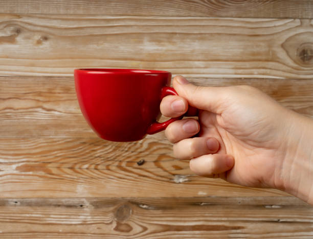 istock Hand Holds Cup, Empty Red Cup in Hands, Coffee Mug, Teacup Mockup, Cup in Arms on Wooden Table 2193668337