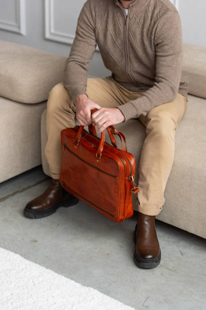 istock A man is comfortably sitting on a sofa, with a leather orange briefcase 2193670454