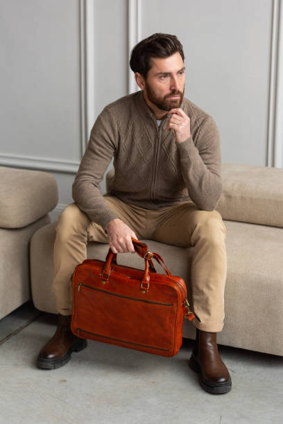 istock A man is comfortably sitting on a sofa, with a leather orange briefcase 2193670722