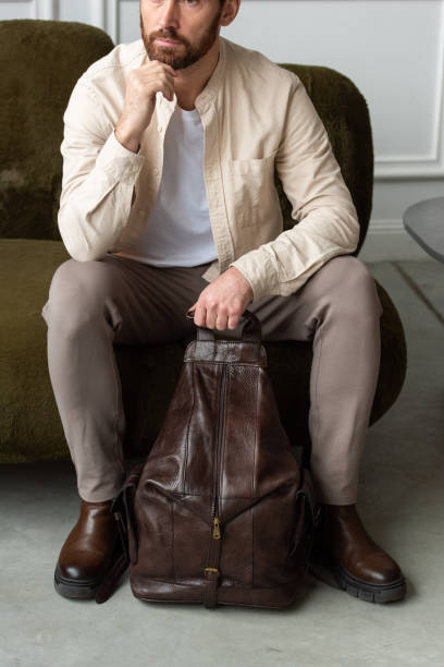 istock A man is comfortably sitting on a sofa, with a leather brown backpack 2193670952