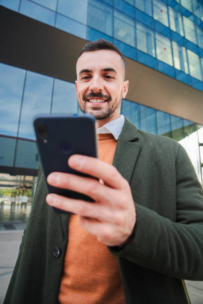 istock Vertical Well dressed guy using banking app with a cellphone. Young business man texting on the social media with a smart phone. Male employee reading an email on his mobile phone at downtown worplace 2193682717