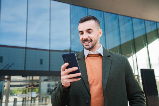 istock Well dressed guy using banking app with a cellphone. Young business man texting on the social media with a smart phone. Male employee reading an email on his mobile phone at downtown worplace 2193683451