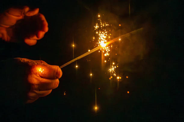 Hand holding burning Christmas sparkler in dark.