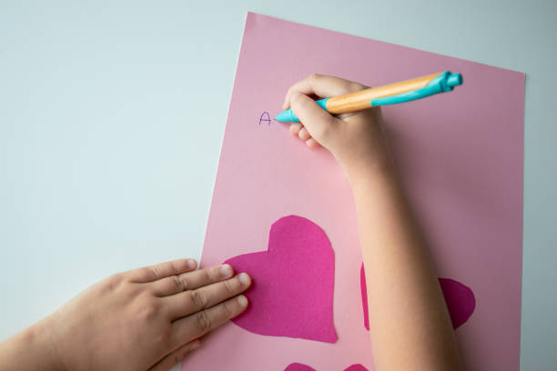 istock Child making heart shaped card with pink paper and letters 2193686873