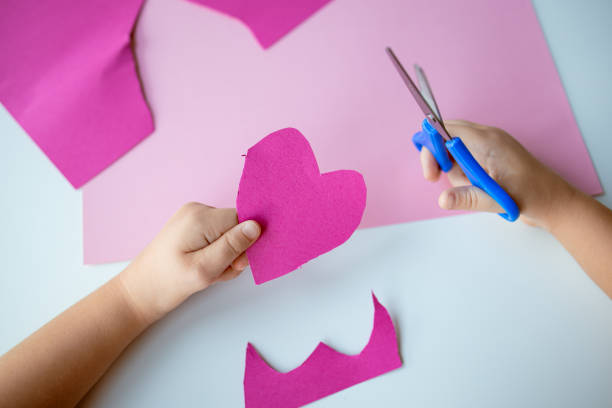istock Child cutting pink heart shape with blue scissors on pink paper 2193686877