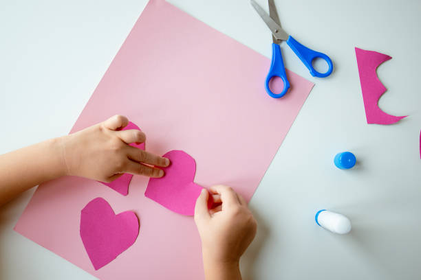 istock Child crafting pink paper hearts with scissors and glue 2193687900