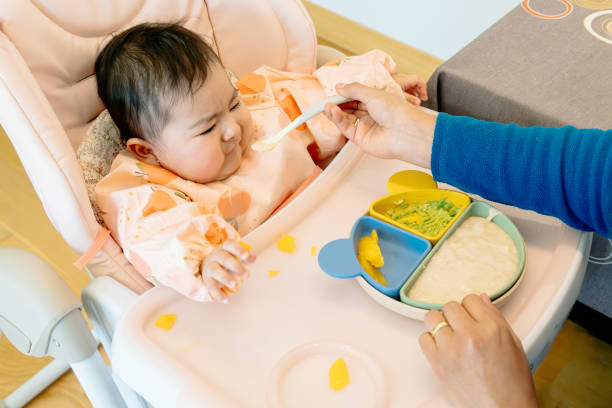 istock Baby crying furiously while being spoon fed sitting in highchair. challenging period for patient and respectful parents. weaning feeding change at 6 months. 2193693444