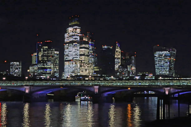 London, United Kingdom, November 26, 2024. City of London financial district skyscrapers illuminated at night. From Southbank of the river Thames. Outdoors on a dark winter night.