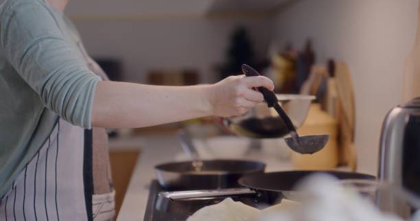 istock Woman Scooping Pancake Batter with Ladle in Kitchen While Cooking 2193697974