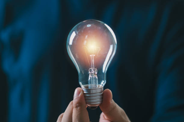 istock Close-up of a lit light bulb held by a hand against a dark background symbolizing innovation, creativity, and bright ideas. 2193698129