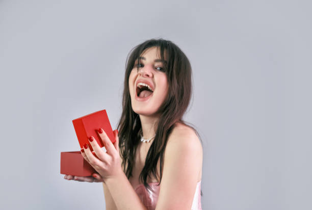 istock A delighted girl opens a gift box, joyfully looking at her present for Valentine's Day celebration. 2193707604