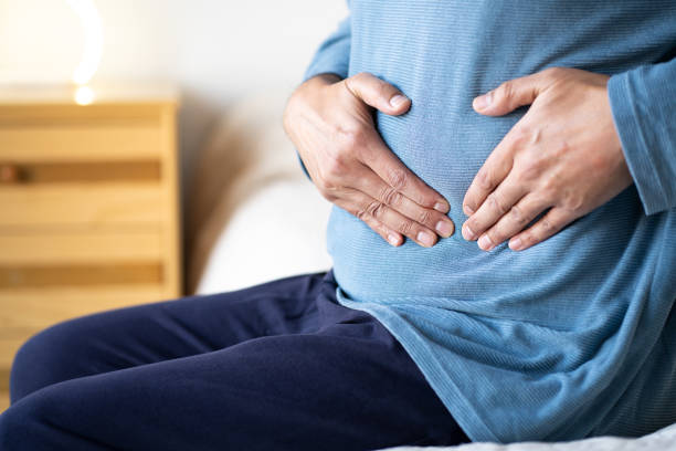 istock Man sitting alone on his bed and suffering from stomach cramps 2193714466