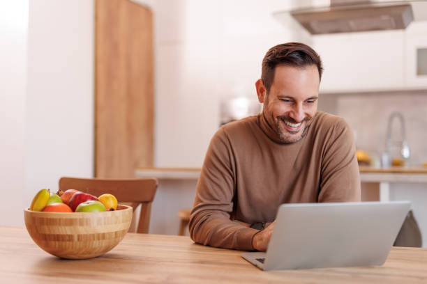 istock Portrait of handsome freelancer smiling and working online over laptop while sitting at dining table 2193720975
