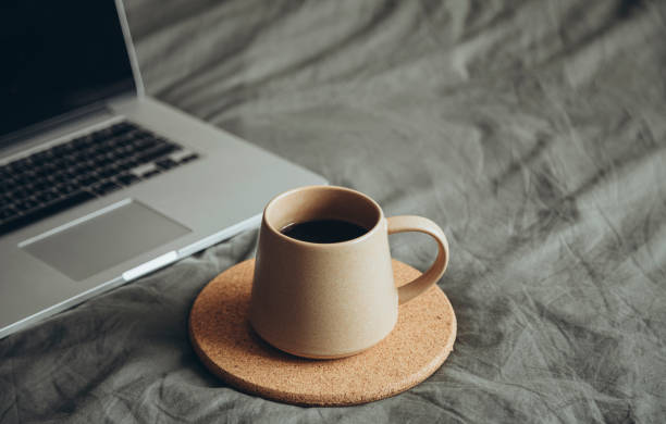 istock Ceramic cup on grey bed in bedroom and laptop on grey bedding near drink. 2193722561