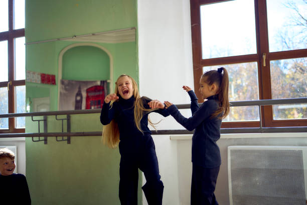 Photo of little ballerinas hugging each other and cheering while practicing together in a ballet studio.