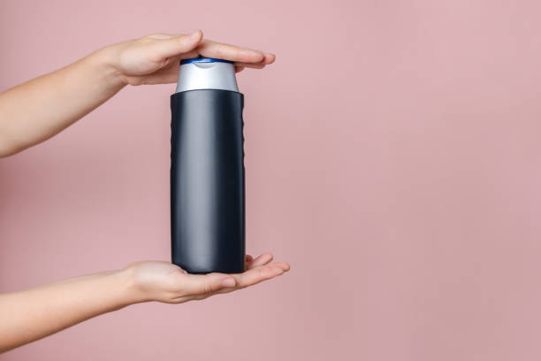 istock Woman's hand holding shampoo bottle on the solid pink background. Cosmetics product package, your brand, spa. Space for text 2193725376