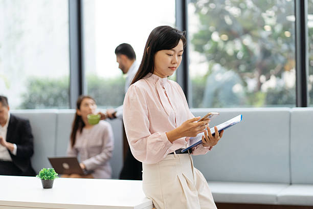 istock Asian businesswoman holding document and using a smartphone while working in a modern office 2193726216