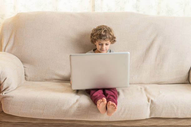 Child sitting on a sofa watching a laptop. Technology concept in childhood.