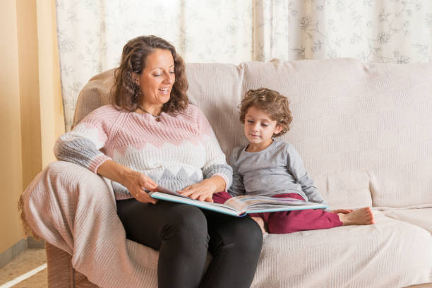 istock Child and a woman sitting on sofa reading a book. 2193735187