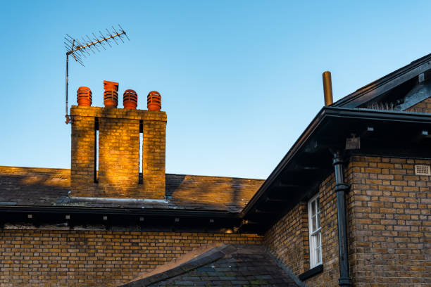 Rooftop of a brick house with chimney, tv antenna, and gutter at sunset
