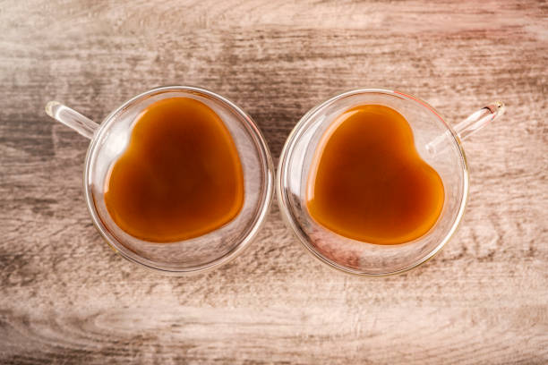 An overhead view of coffee in two heart shaped glass cups on a table top.