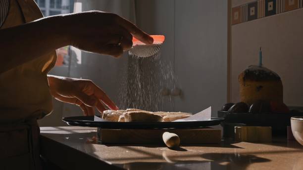 istock Woman Sprinkling Powdered Sugar on Easter Cookies in a Kitchen 2193751768