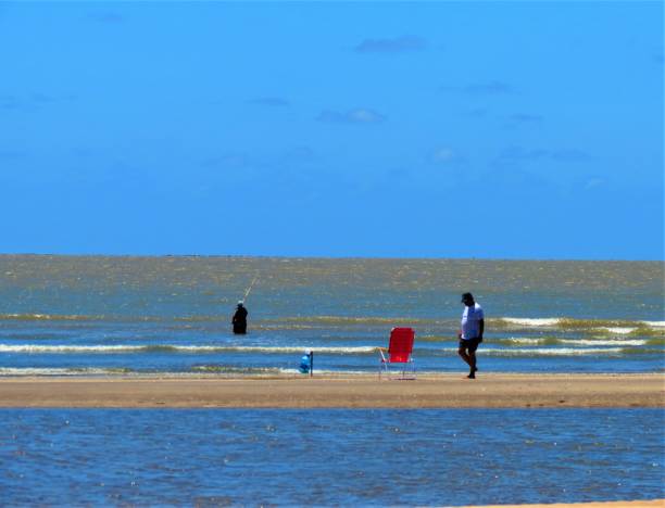 San Clemente del Tuyú, Buenos Aires Province, Argentina - People relaxing at the Punta Rasa beach. Punta Rasa is one of those few places in the world where a curious phenomenon occurs: the sun rises over the sea and sets over the river. And all this spectacle can be seen from the spit of sand that receives the name of Punta Rasa and that goes into the water to become the southern end of Samborombón Bay and the northern end of Cape San Antonio, just where they merge. the river with the sea. Punta Rasa is a lighthouse, a biological station.This place, where the wind blows practically all year round, has the privilege of having gigantic concentrations of birds of different species in migration, which come from places in the northern hemisphere -such as Alaska, Canada or the Salvador Peninsula- to rest, gain weight. and continue their journey to Tierra del Fuego, from where they begin their return with the arrival of autumn.