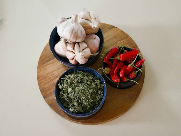 Dried Cayenne peppers, dried Oregano and fresh garlic laying on a wooden chopping board. Culinary aromatics. Cooking background. Flavourful spices. Herbs and spices.